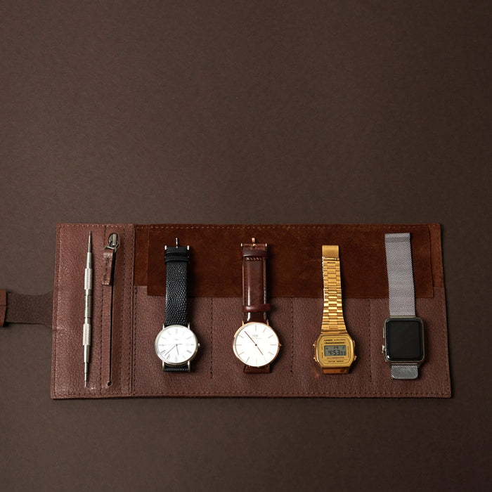 Brown leather watch roll laid open with four watches and tools